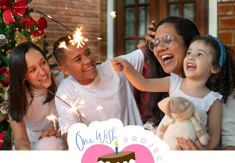 A family embraces and plays with sparklers with the One Wish Project logo embedded in the foreground