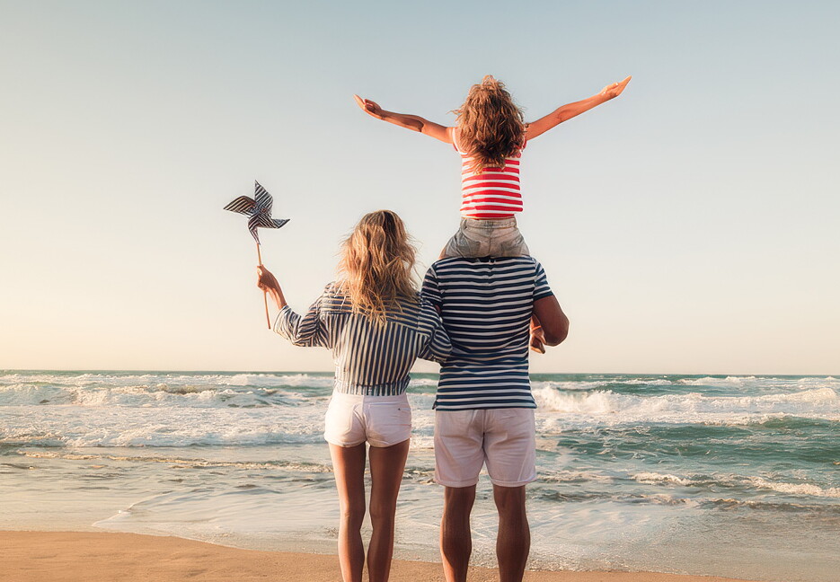 A couple stands on the PLymouth beach with a child on the father's shoulders.