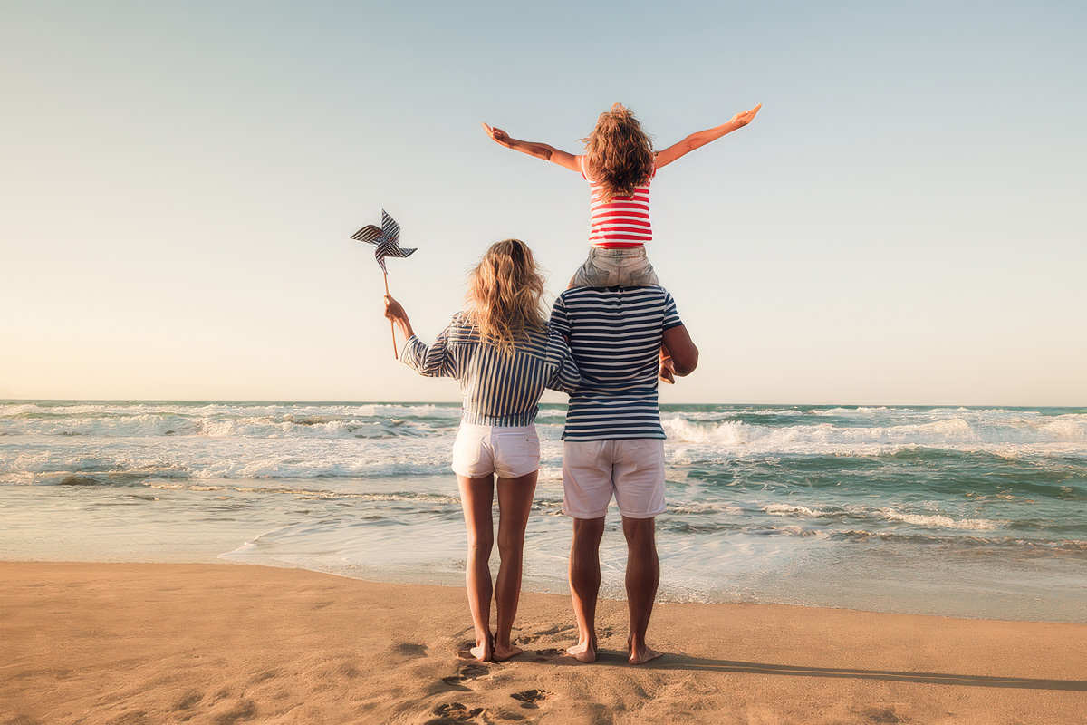 A couple stands on the PLymouth beach with a child on the father's shoulders.